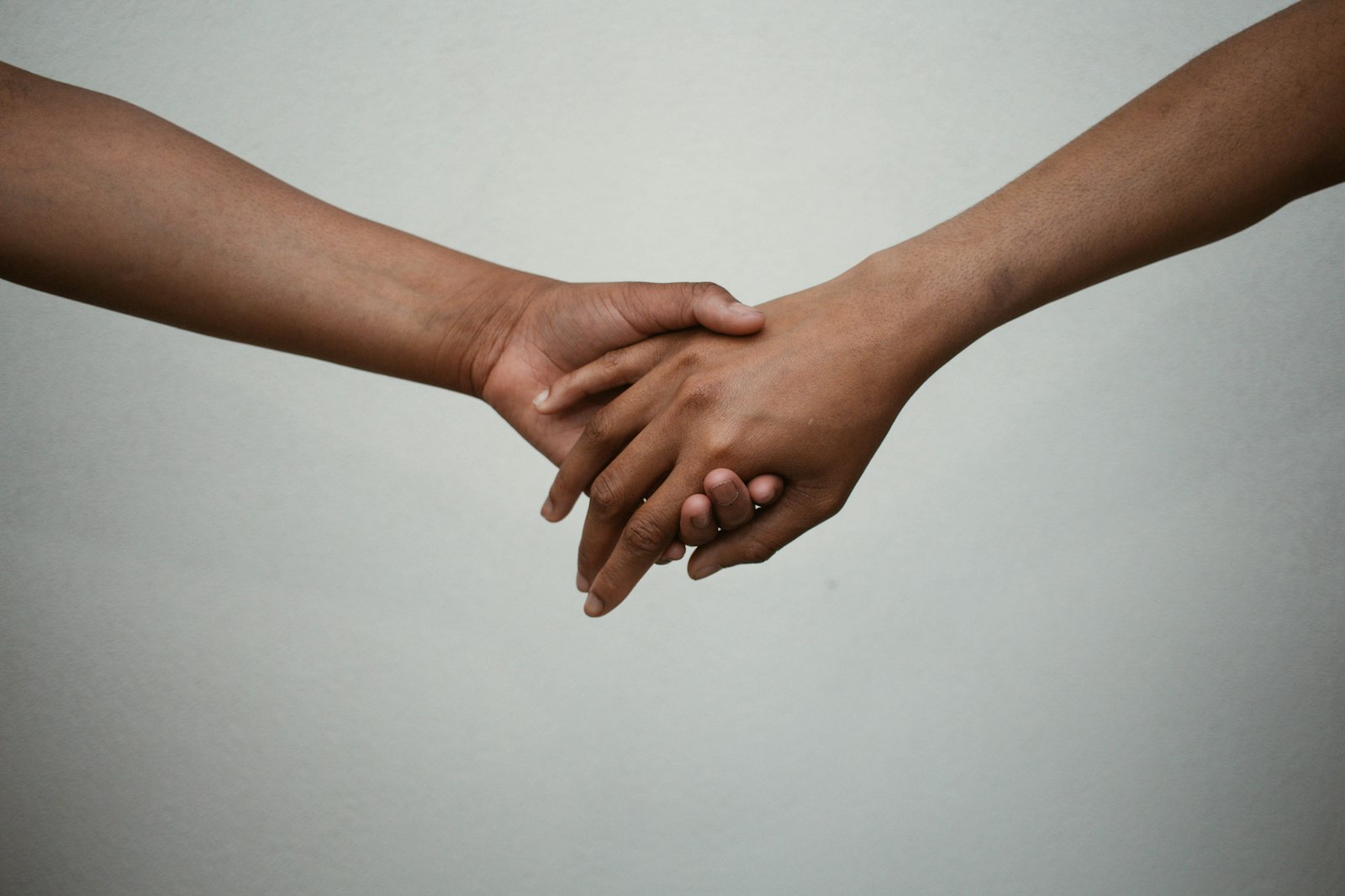 Two people reaching toward each other and clasping hands against a soft neutral background.